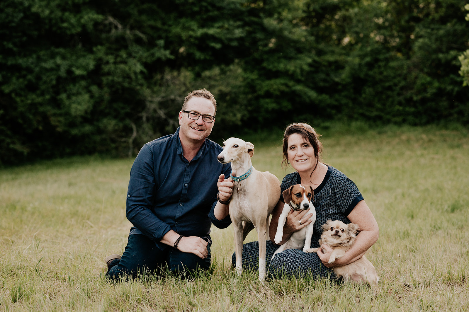 Michaela und Peter sitzen mit ihren drei Hunden auf einer Wiese bei La Bastide